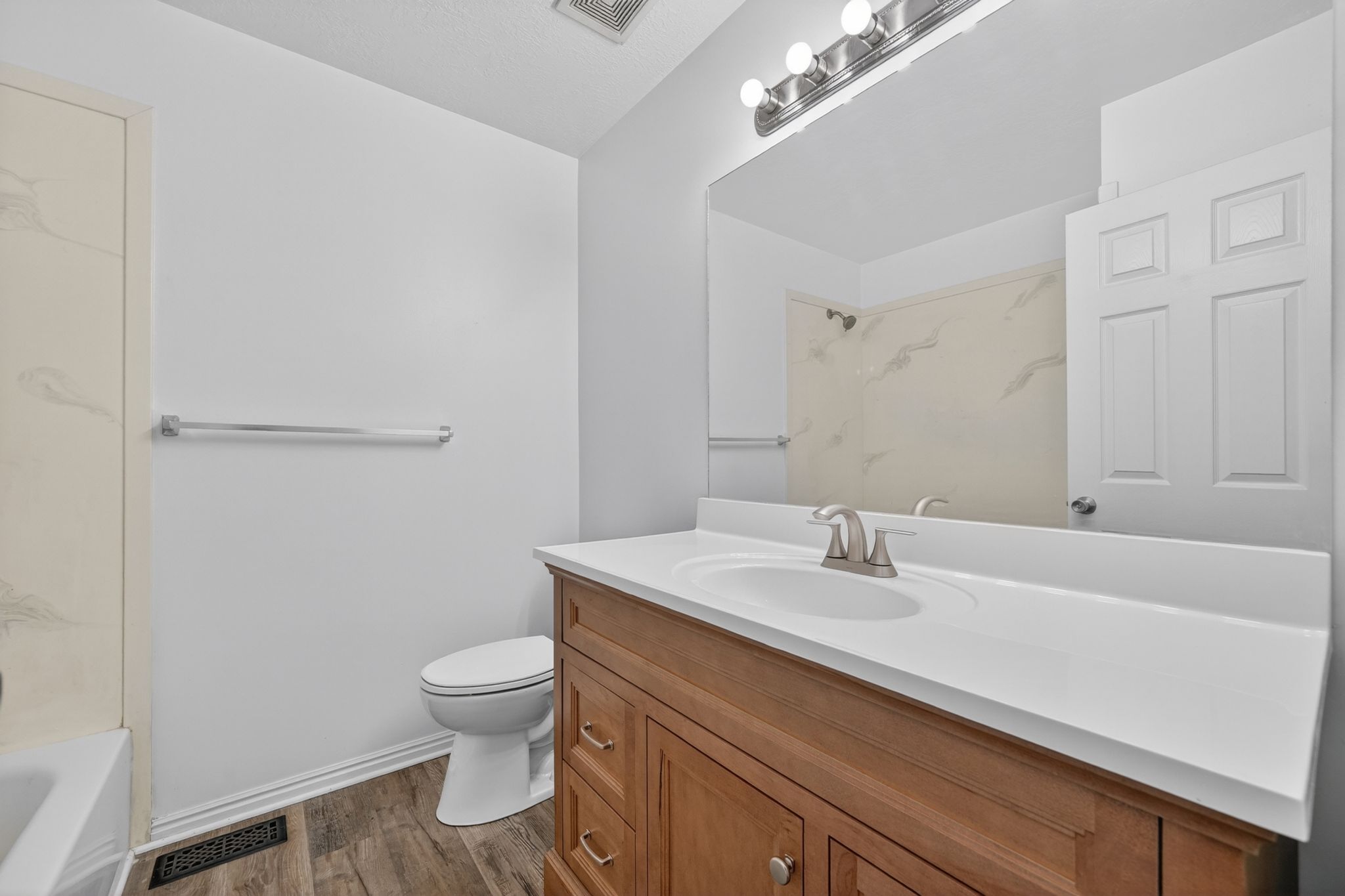 Bathroom featuring a wood-finish vanity with a white countertop and integrated sink, brushed nickel faucet, large wall mirror, and a three-light vanity fixture