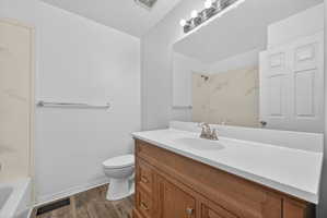 Bathroom featuring a wood-finish vanity with a white countertop and integrated sink, brushed nickel faucet, large wall mirror, and a three-light vanity fixture