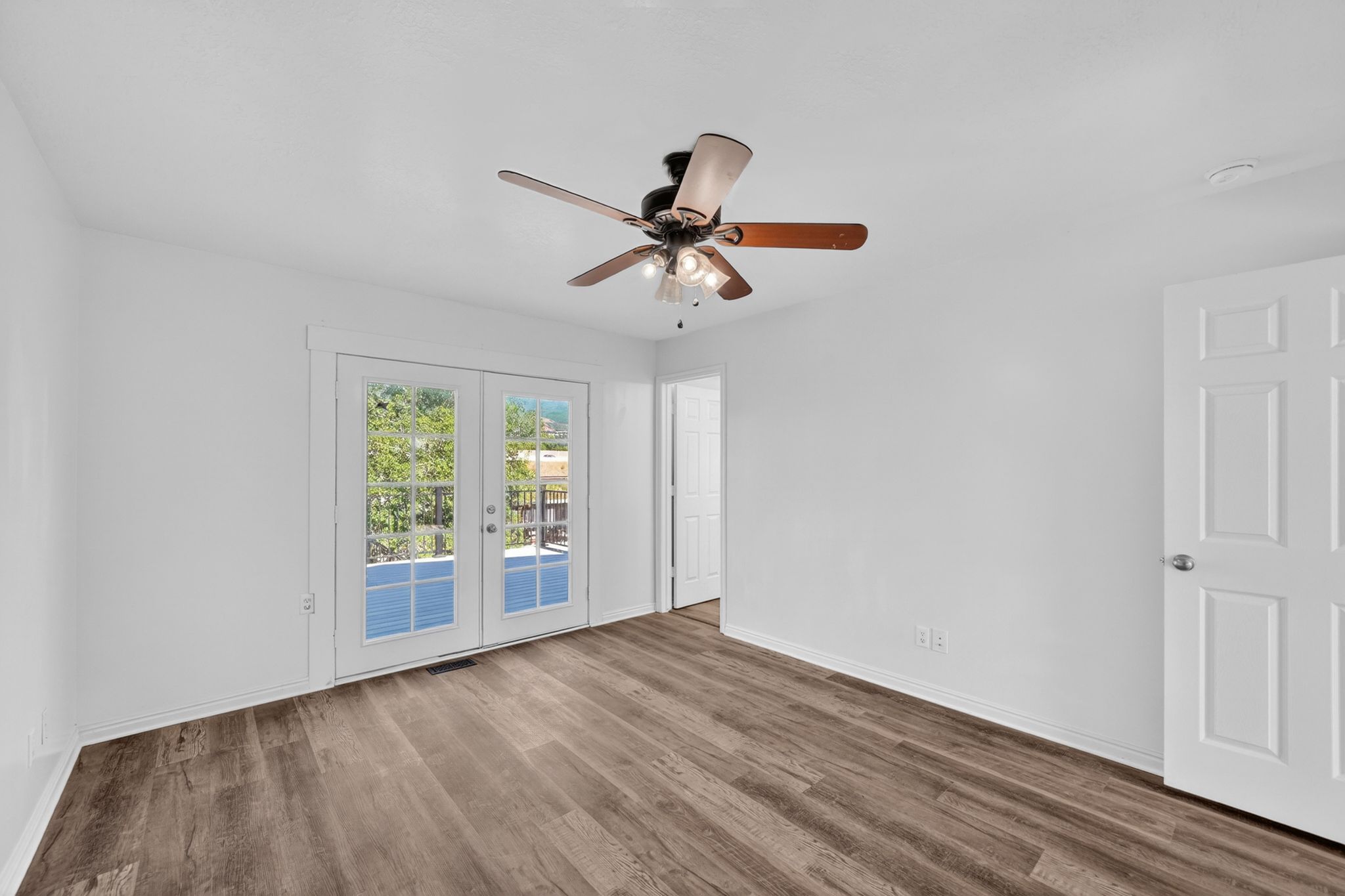 Wood-finish flooring throughout, white baseboards, and a ceiling fan with integrated lighting