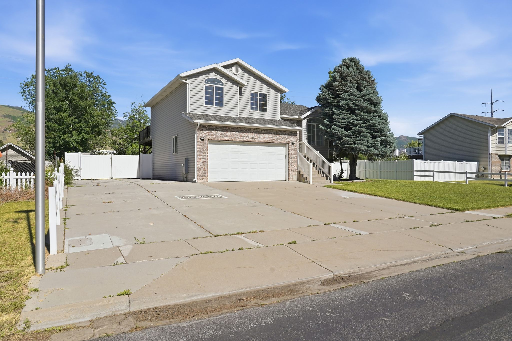 Two-story residence featuring light gray siding, a prominent two-car garage with a white door, and a partial brick facade