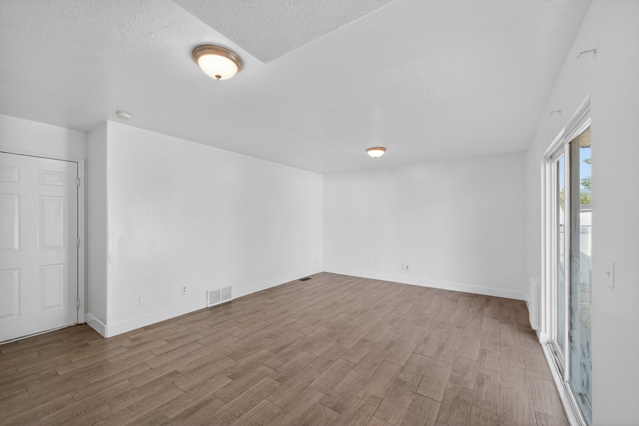Spacious room featuring wood-finish flooring, white walls, and a recessed ceiling light