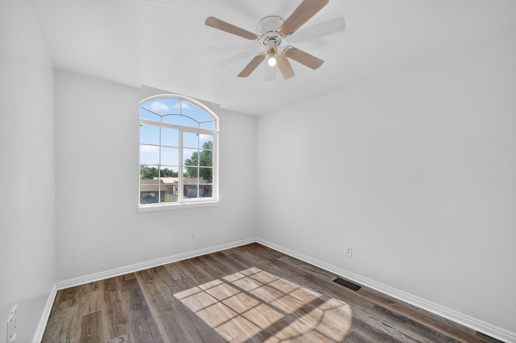 Arch-top window, wood-finish flooring, ceiling fan, and white baseboards