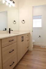 Bathroom vanity featuring light wood-finish cabinetry with black hardware, a light-toned countertop, and an integrated sink with a matte black faucet