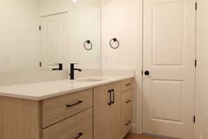 Bathroom vanity featuring a light wood-finish cabinet with matte black hardware, a light-toned countertop, and an undermount sink with a matte black faucet