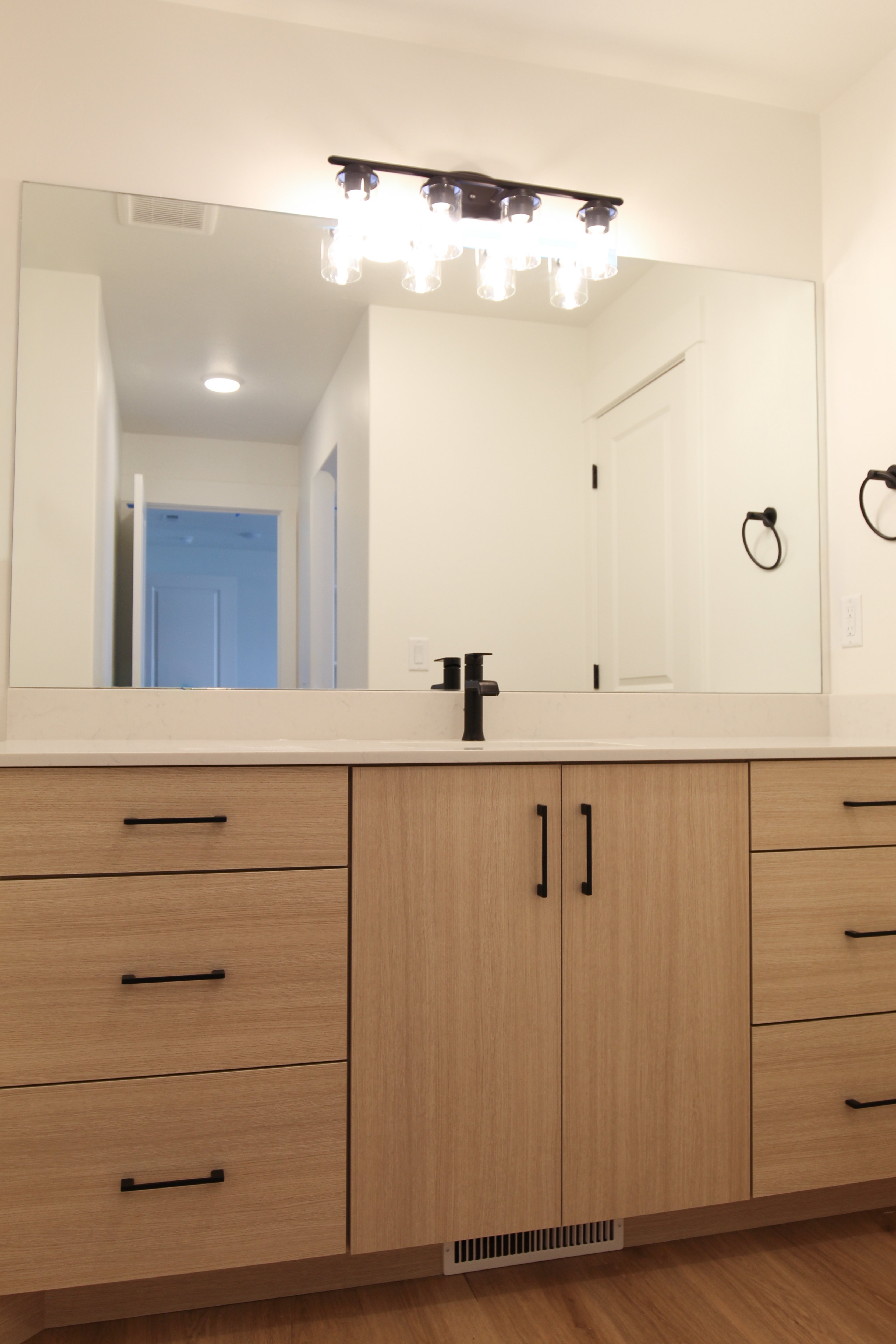 Bathroom vanity featuring light wood-finish cabinetry, a white countertop, a wide mirror, and a contemporary black faucet