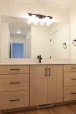 Bathroom vanity featuring light wood-finish cabinetry, a white countertop, a wide mirror, and a contemporary black faucet