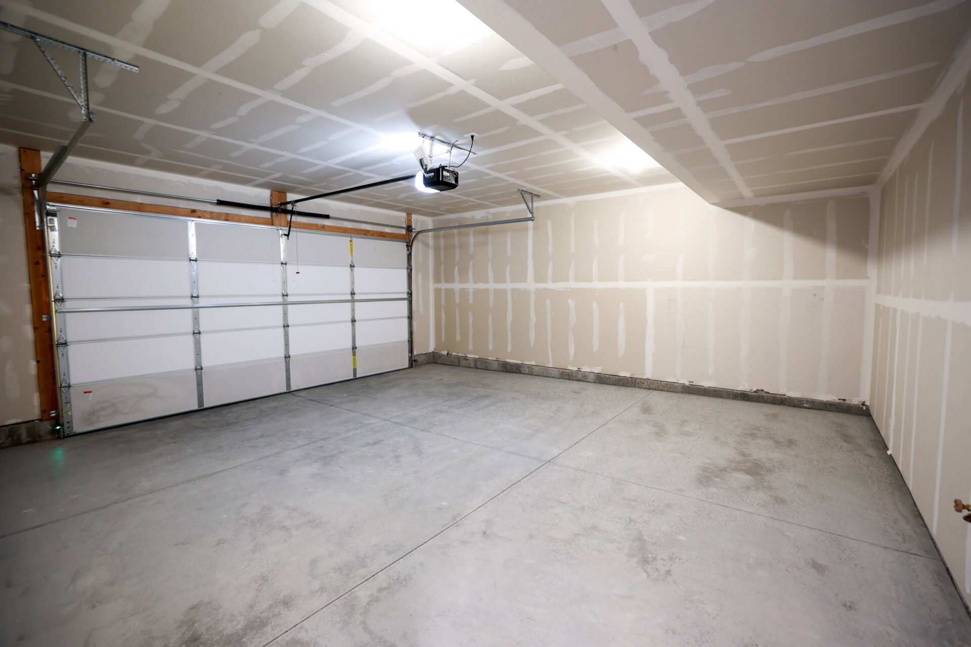 Spacious garage featuring a concrete floor, overhead lighting, an automatic garage door opener, and a panel-style garage door