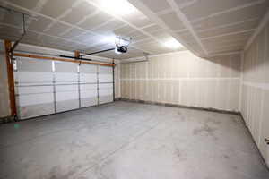 Spacious garage featuring a concrete floor, overhead lighting, an automatic garage door opener, and a panel-style garage door