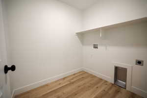 Dedicated laundry space featuring wood-finish flooring, crisp white walls, a built-in shelving unit, and plumbing hookups