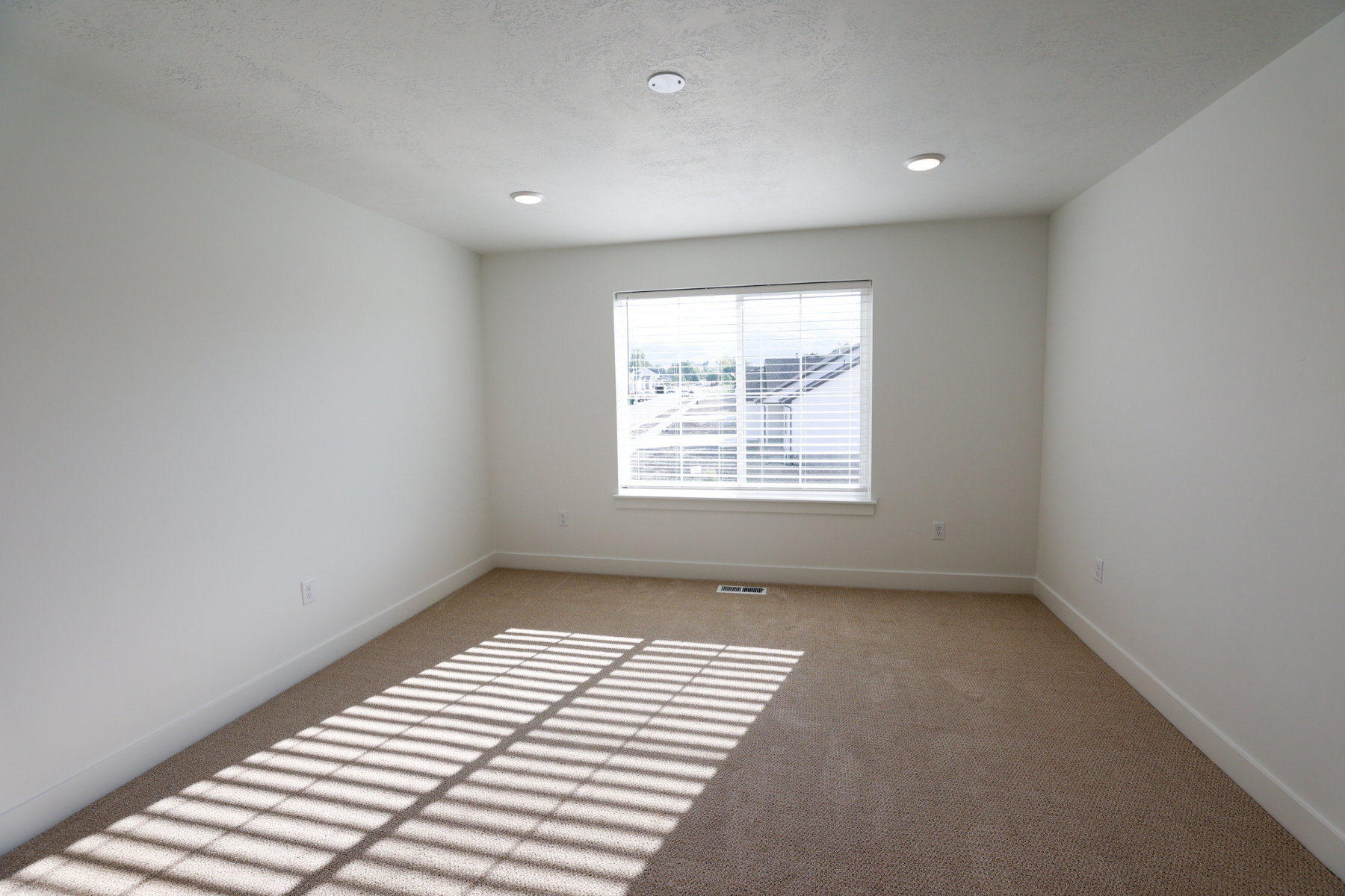 Neutral-toned carpeting paired with white walls, a single window featuring horizontal blinds, and recessed lighting