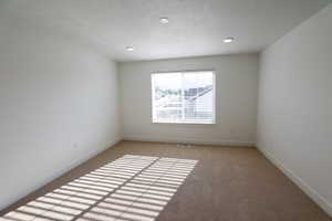 Neutral-toned carpeting paired with white walls, a single window featuring horizontal blinds, and recessed lighting