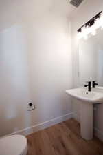 Modern powder room featuring a white pedestal sink, black matte faucet, and wood-finish flooring