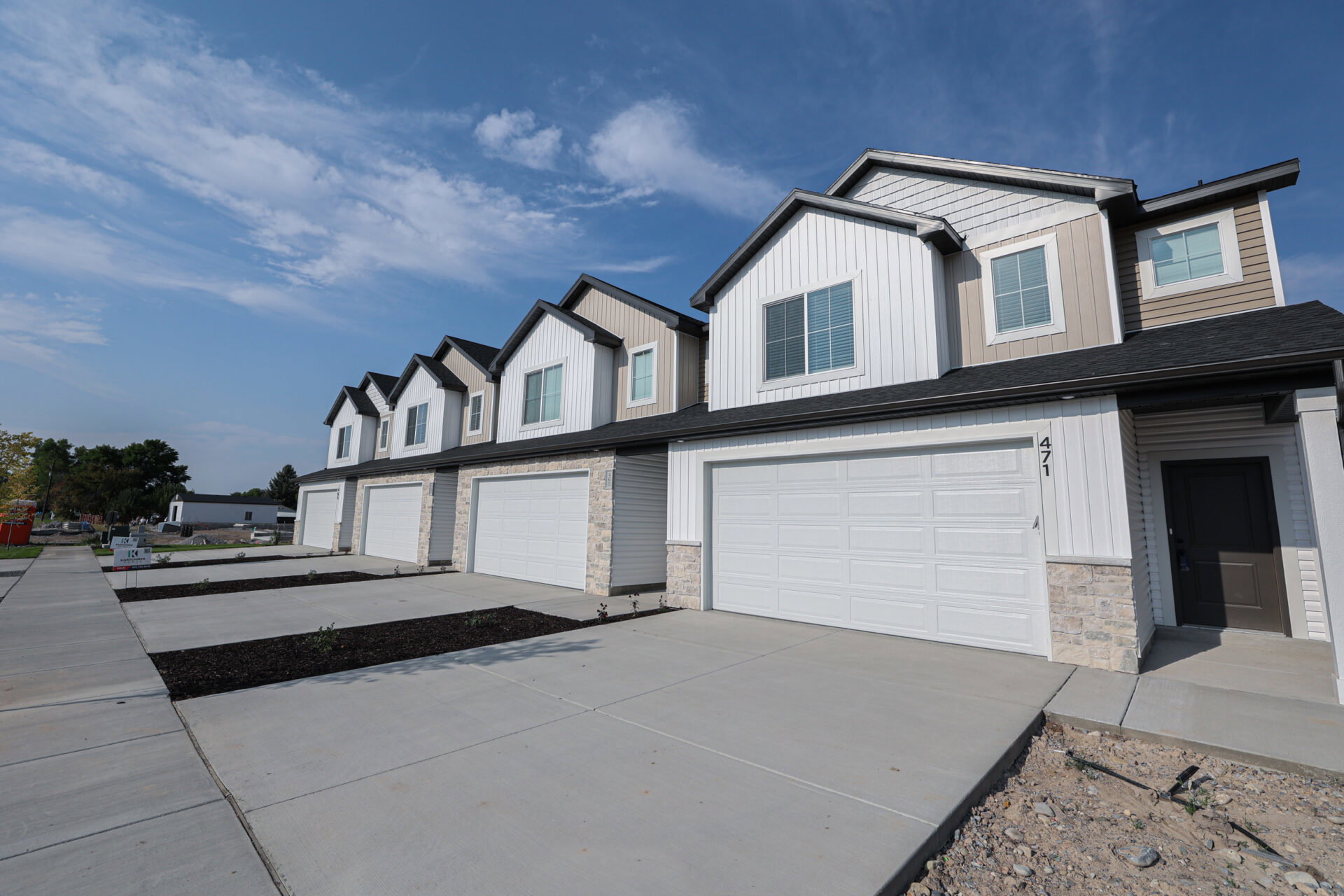 Contemporary townhome exterior featuring vertical and horizontal siding, stone accents, a two-car garage, and a dark entry door
