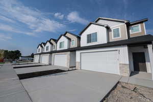 Contemporary townhome exterior featuring vertical and horizontal siding, stone accents, a two-car garage, and a dark entry door