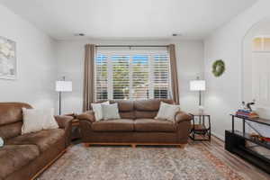 Living area featuring wood-finish flooring, white walls, and a large window with plantation shutters