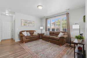 Living area featuring wood-finish flooring, light neutral wall paint, and a large window with white plantation shutters