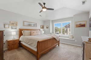 Carpeted bedroom featuring a tray ceiling, ceiling fan, and a window seat with plantation shutters
