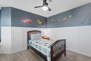 Bedroom featuring board and batten wainscoting, carpet flooring, a ceiling fan with integrated lighting, and a corner window ledge