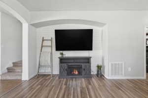 Living area featuring wood-finish flooring, a built-in electric fireplace with shiplap accent wall, and arched doorways