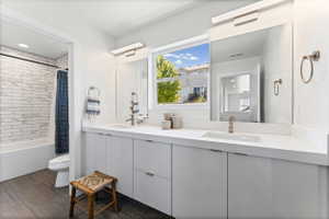 Bathroom featuring a dual vanity with white cabinetry and integrated sinks, under-mirror lighting, and wood-finish flooring