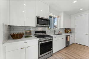 Modern kitchen featuring white flat-panel cabinetry, stainless steel appliances, a subway tile backsplash, light-toned countertops, and wood-finish flooring