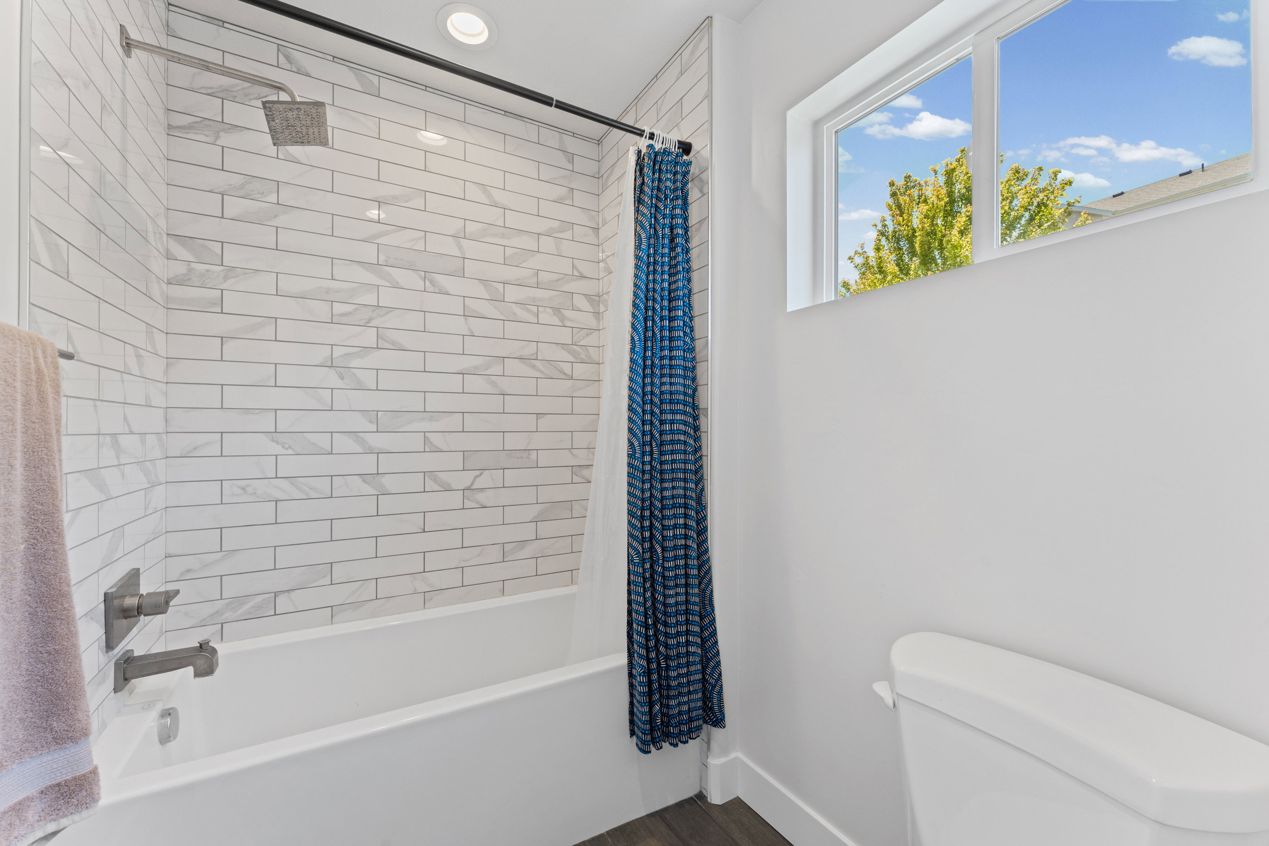 Bathroom featuring white subway tile shower surround with geometric accents, brushed nickel fixtures, a white soaking tub, and a window providing natural light