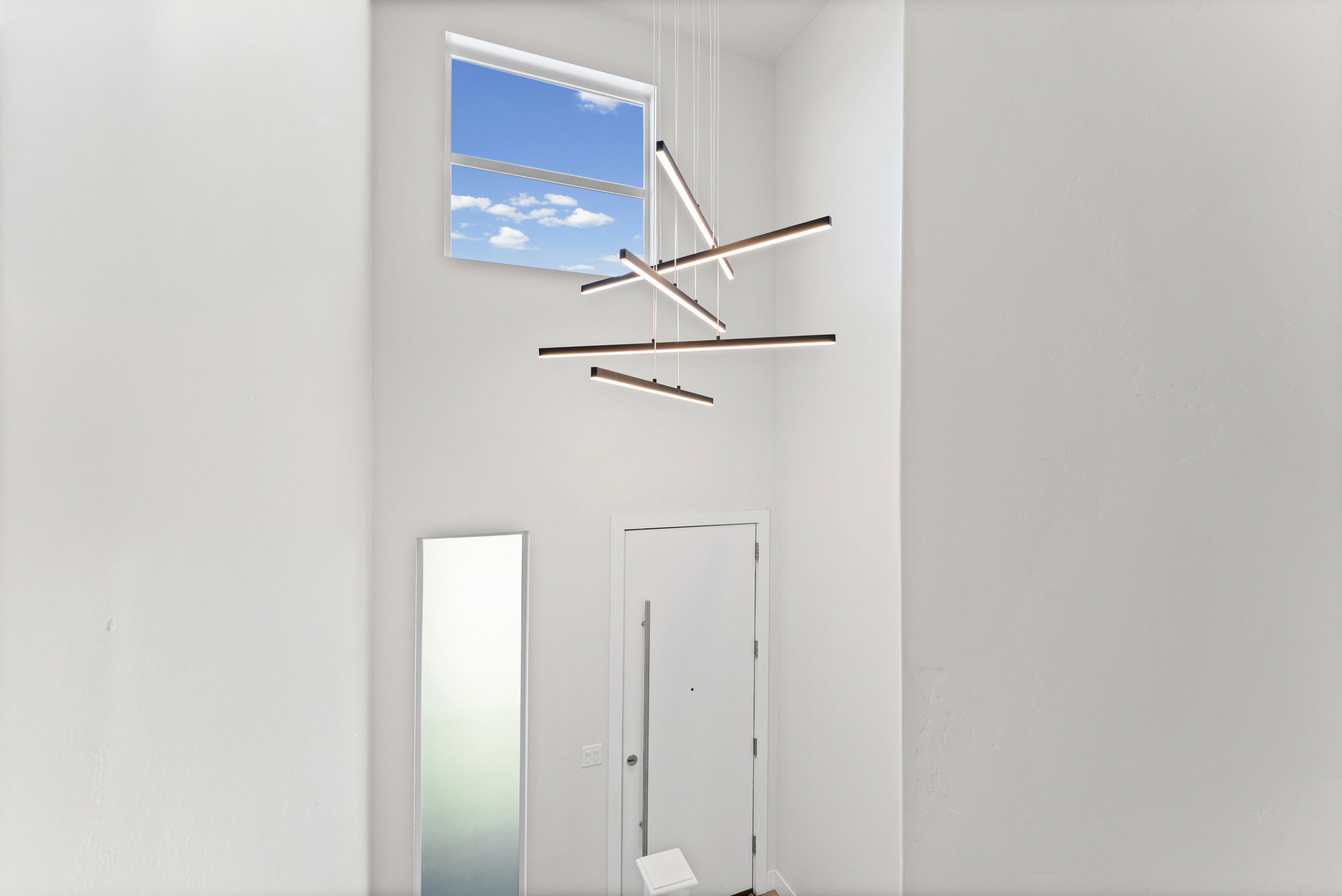 Two-story entry featuring high ceilings, a contemporary linear chandelier, a transom window, and a white entry door with a horizontal pull handle