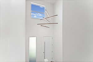 Two-story entry featuring high ceilings, a contemporary linear chandelier, a transom window, and a white entry door with a horizontal pull handle