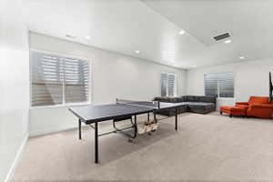 Spacious recreation room featuring light-toned carpeting and multiple windows with horizontal blinds