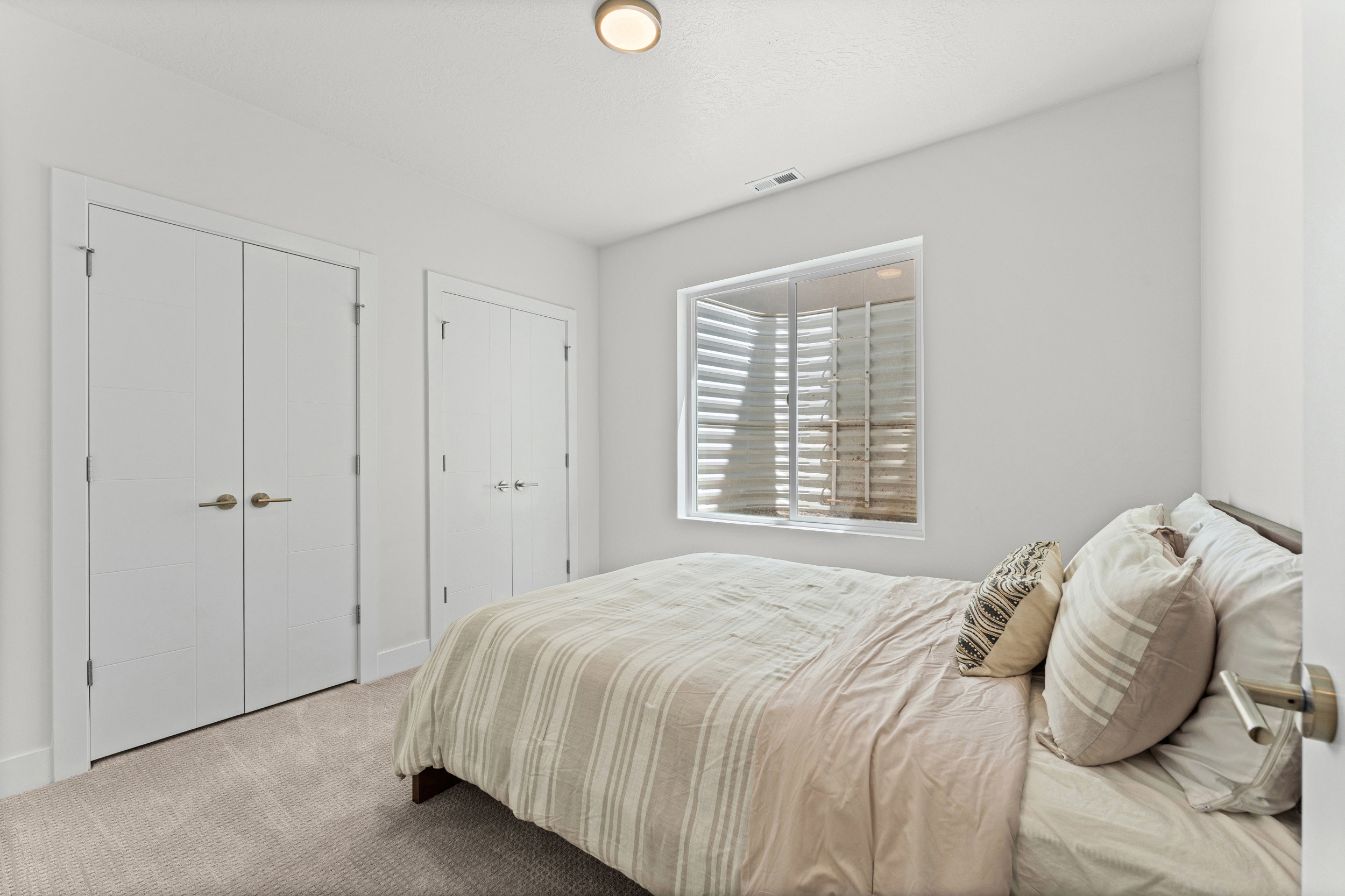 Room featuring neutral wall tones, carpet flooring, a window with plantation shutters, a flush-mount ceiling light, and two bifold closet doors