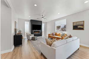 Open-concept living space with wood-finish flooring, a contemporary fireplace feature wall, recessed lighting, and a ceiling fan