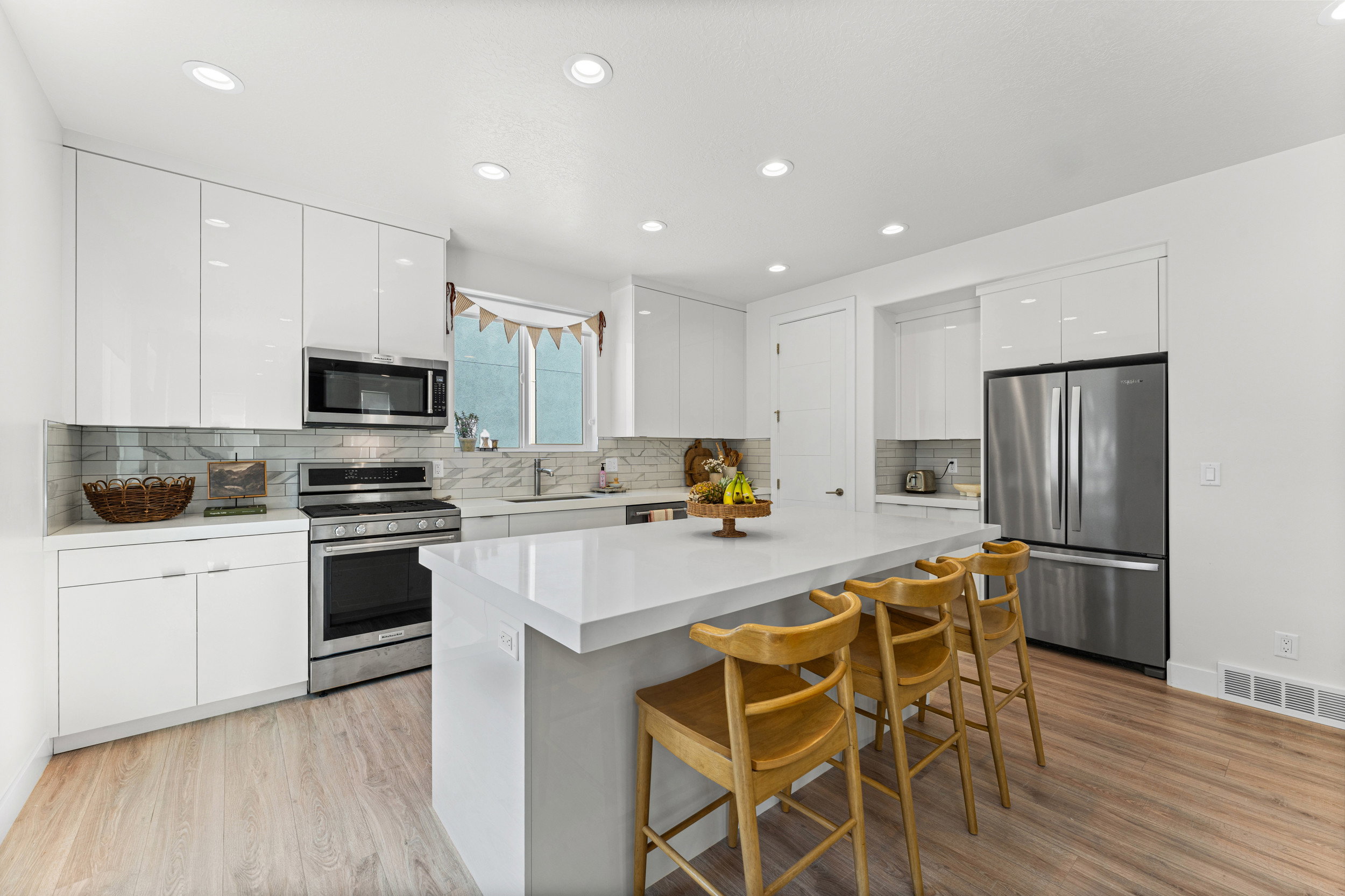 Contemporary kitchen featuring high-gloss white cabinetry, stainless steel appliances, a white waterfall island, wood-finish flooring, and recessed lighting