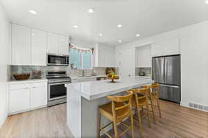 Contemporary kitchen featuring high-gloss white cabinetry, stainless steel appliances, a white waterfall island, wood-finish flooring, and recessed lighting