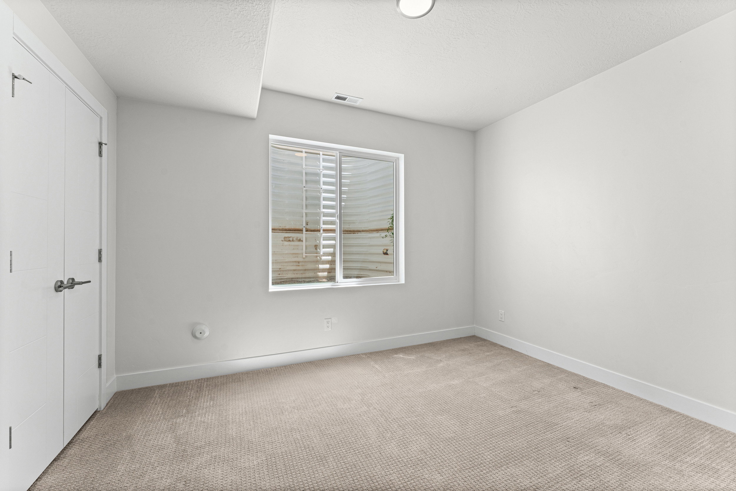 Carpeted interior space featuring white walls and a large window with blinds