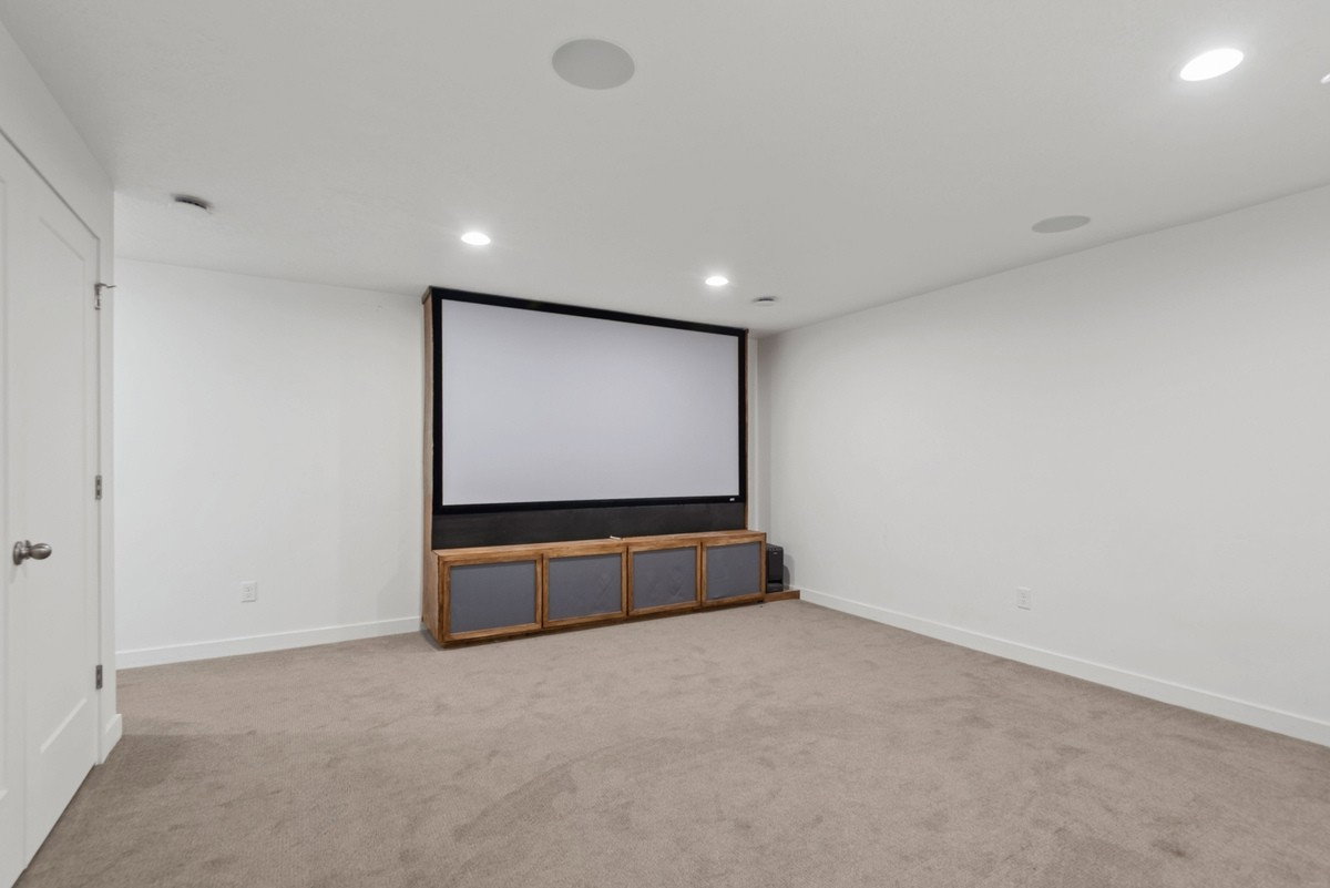 Dedicated media room featuring a large projection screen, built-in media console, recessed lighting, integrated ceiling speakers, and neutral carpet flooring