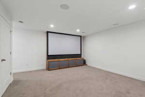 Dedicated media room featuring a large projection screen, built-in media console, recessed lighting, integrated ceiling speakers, and neutral carpet flooring
