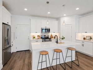 Kitchen featuring a central island with a matte black faucet, white shaker-style cabinetry, stainless steel appliances, wood-finish flooring, and pendant lighting