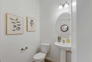Bathroom featuring a pedestal sink with a single-handle faucet, oval mirror, and a two-bulb vanity light fixture