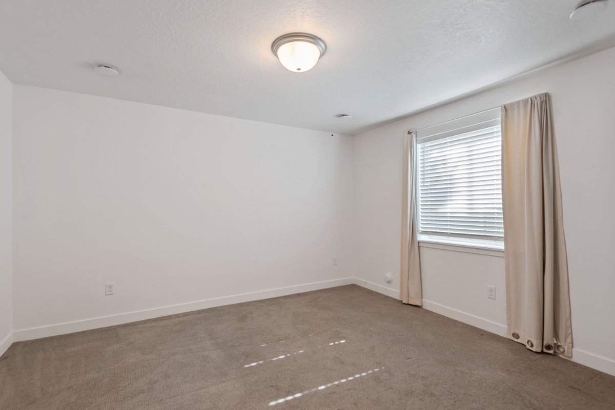 Carpeted room featuring a single window with blinds and drapes, a flush-mount ceiling light fixture, and white baseboards