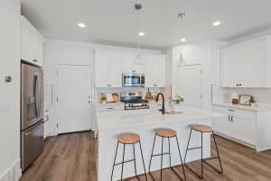 Modern kitchen featuring a central island, white shaker cabinetry, stainless steel appliances, wood-finish flooring, and subway tile backsplash