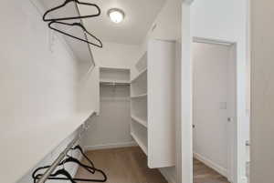 Walk-in closet featuring built-in shelving, multiple hanging rods, and wood-finish flooring