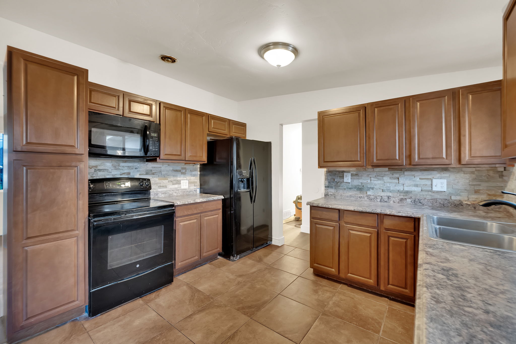 Kitchen with wood-finish cabinetry, black appliances, textured tile backsplash, and stone-finish countertops