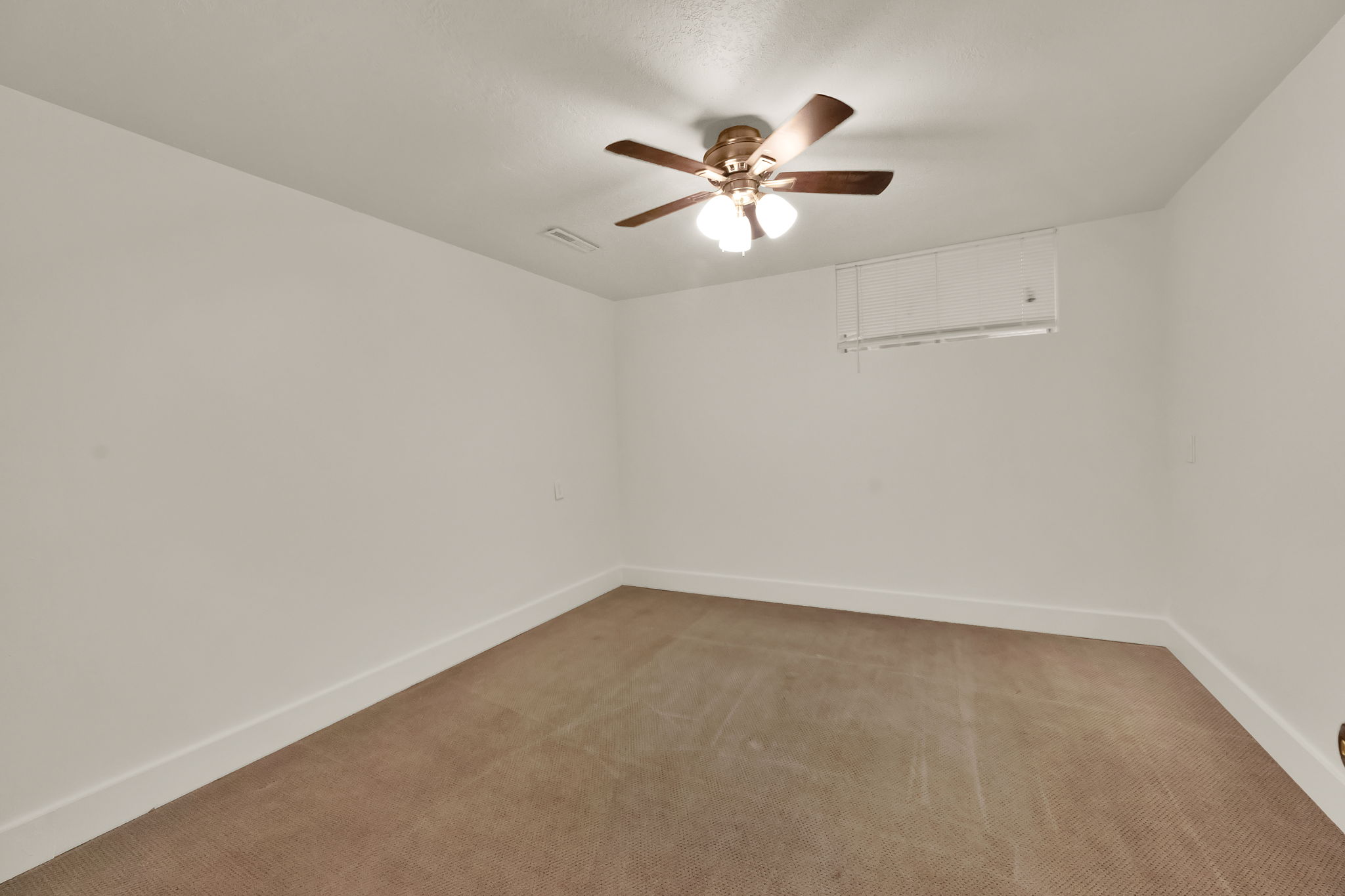 Carpeted room featuring a ceiling fan with integrated lighting, white walls, and clean white baseboards