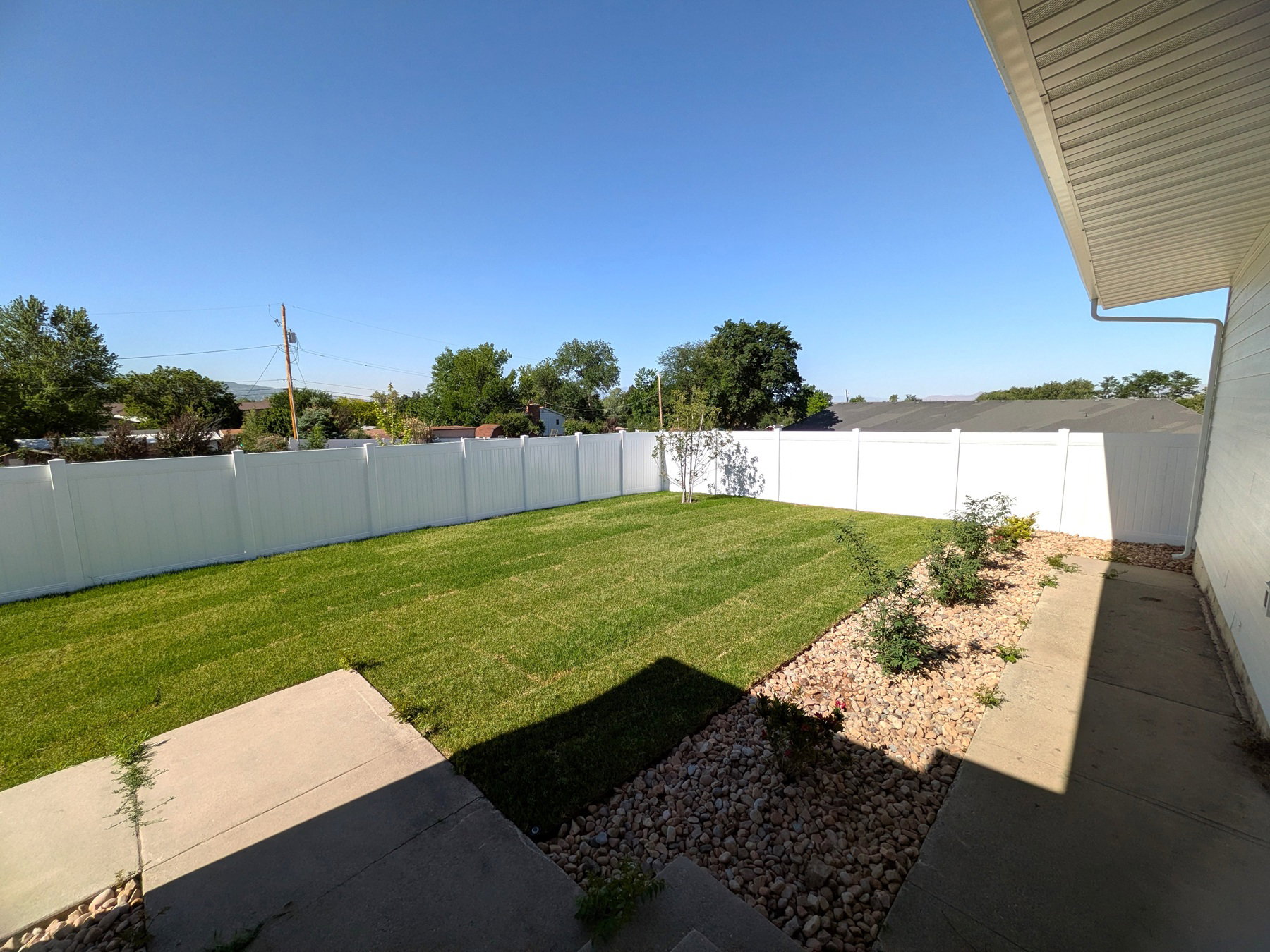 Expansive backyard featuring a lush lawn, white privacy fencing, and a decorative rock border with small plantings