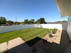 Expansive backyard featuring a lush lawn, white privacy fencing, and a decorative rock border with small plantings