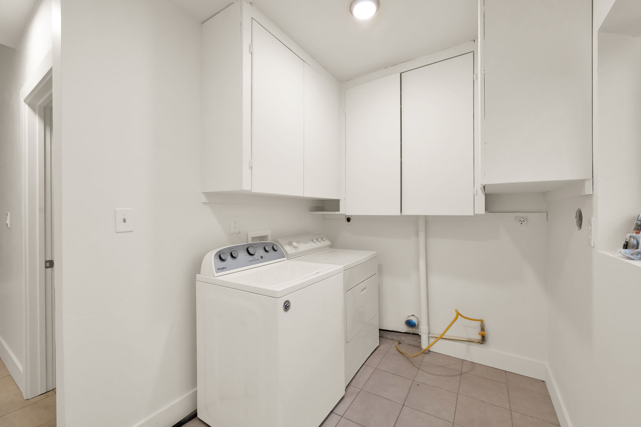 Dedicated laundry area featuring white cabinetry for storage and tile flooring