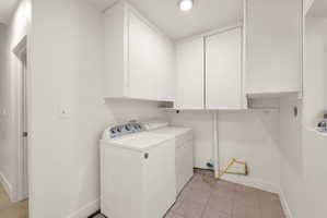 Dedicated laundry area featuring white cabinetry for storage and tile flooring