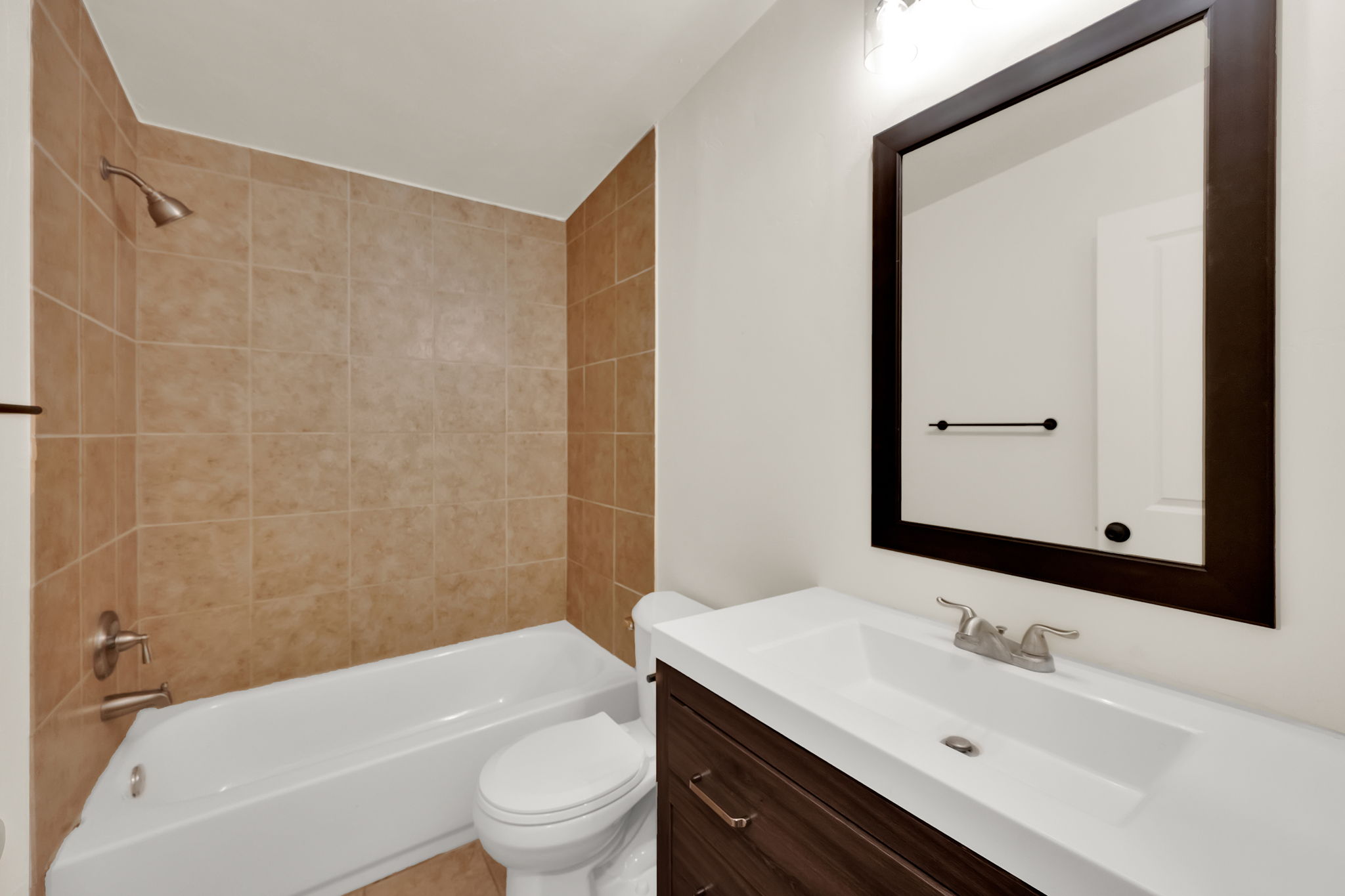 Full bathroom featuring a white tub, shower with tan tile surround, and a dark wood-finish vanity with an integrated white sink and counter