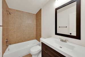 Full bathroom featuring a white tub, shower with tan tile surround, and a dark wood-finish vanity with an integrated white sink and counter