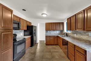 U-shaped kitchen featuring wood cabinetry, integrated black appliances, stone-look countertops, and a full-height tile backsplash